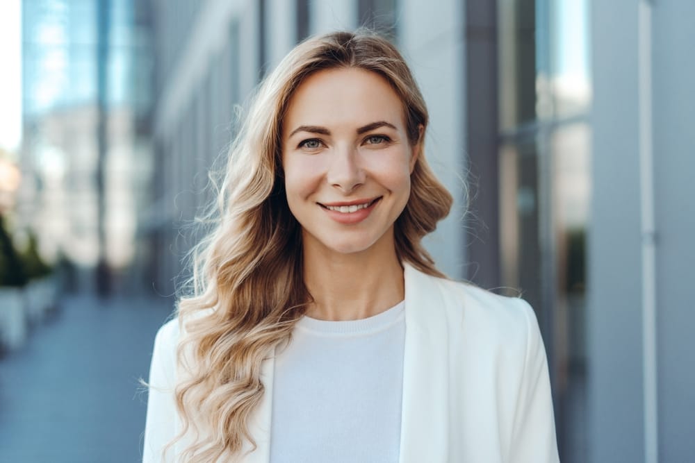 Smiling woman with long blonde hair and clear eyesight standing outdoors near modern buildings, showcasing confidence after LASIK surgery – LASIK Houston TX